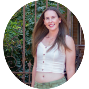 A woman posing in front of plants behind a wrought iron fence.