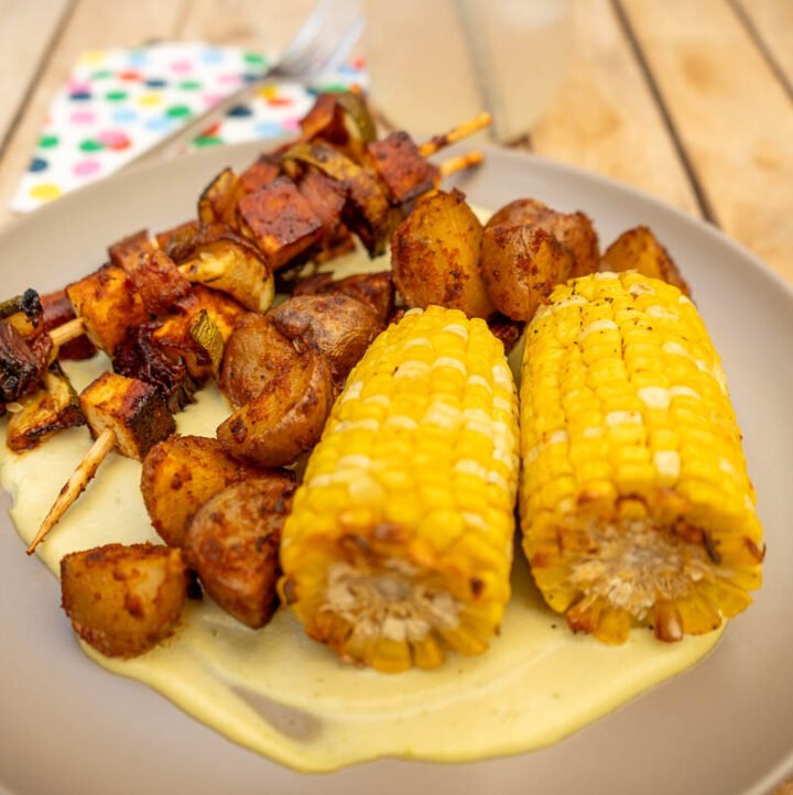 Close up of corn on the cob, potatoes, and tofu skewers on a plate.