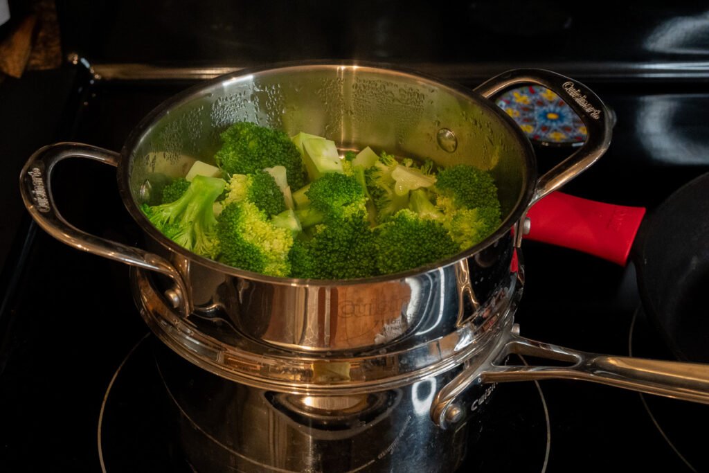 A stainless steel double boiler with steamed broccoli.