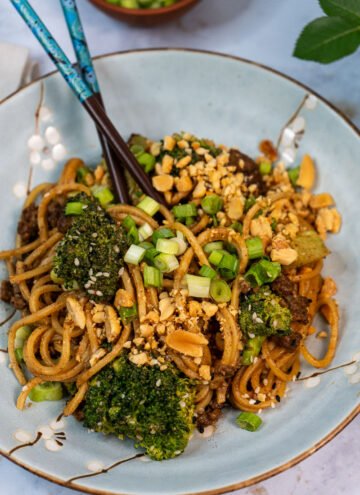 Close up of a bowl of "beef" and broccoli noodles. There are chopsticks sticking out of the noodles.