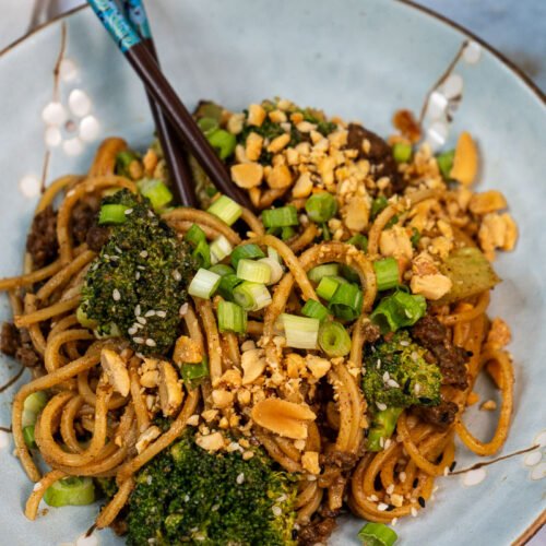 Close up of a bowl of "beef" and broccoli noodles. There are chopsticks sticking out of the noodles.