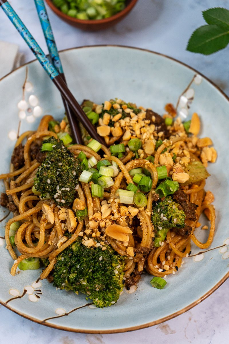 Close up of a bowl of "beef" and broccoli noodles. There are chopsticks sticking out of the noodles.