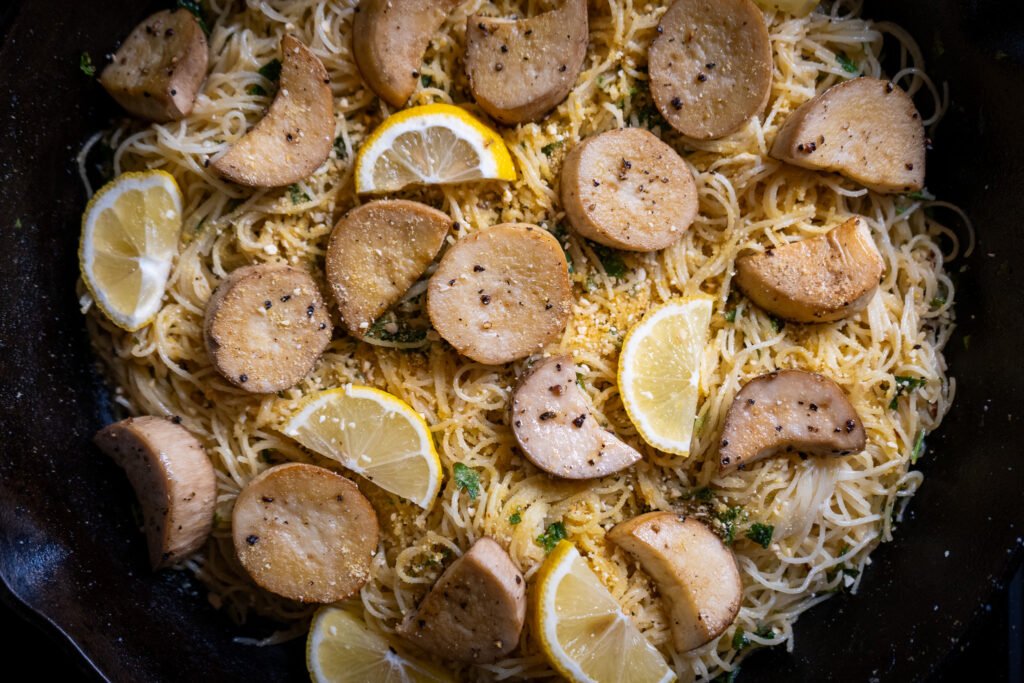 Close up of angel hair pasta dish with vegan scallops in a cast iron pan.