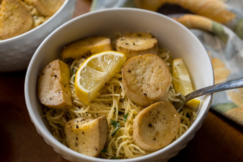 A white bowl of angel hair pasta and vegan scallops with a fork in it.