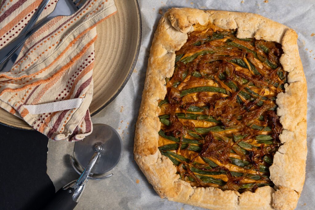 The green bean and caramelized onion galette cooked. There are two plates to the left and a pizza cutter.