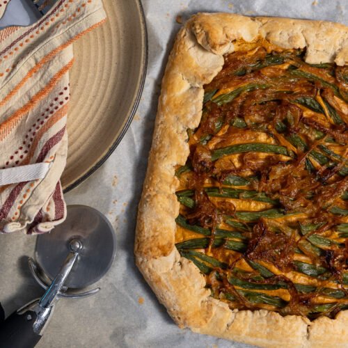 The green bean and caramelized onion galette cooked. There are two plates to the left and a pizza cutter.