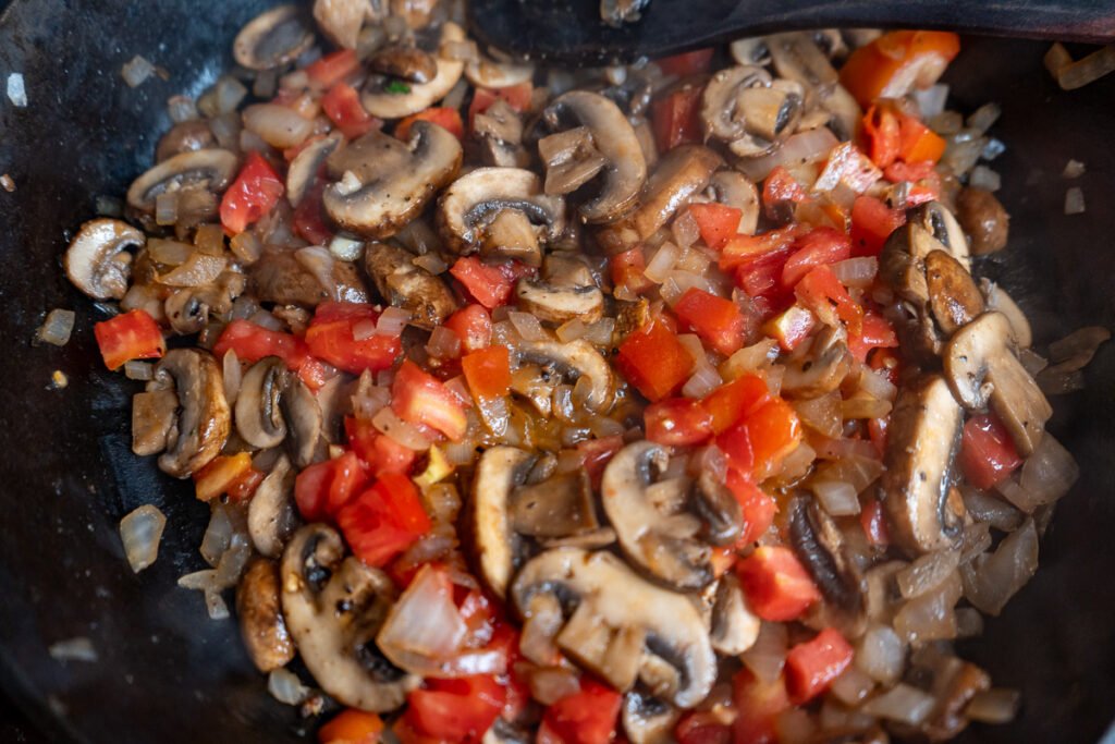 Onion, tomato, and mushrooms sauteed in a cast iron pan.