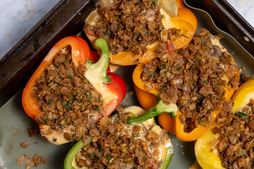 Close up of bell peppers cut in half lengthwise and stuffed with frittata and vegan sausage uncooked on a baking sheet.