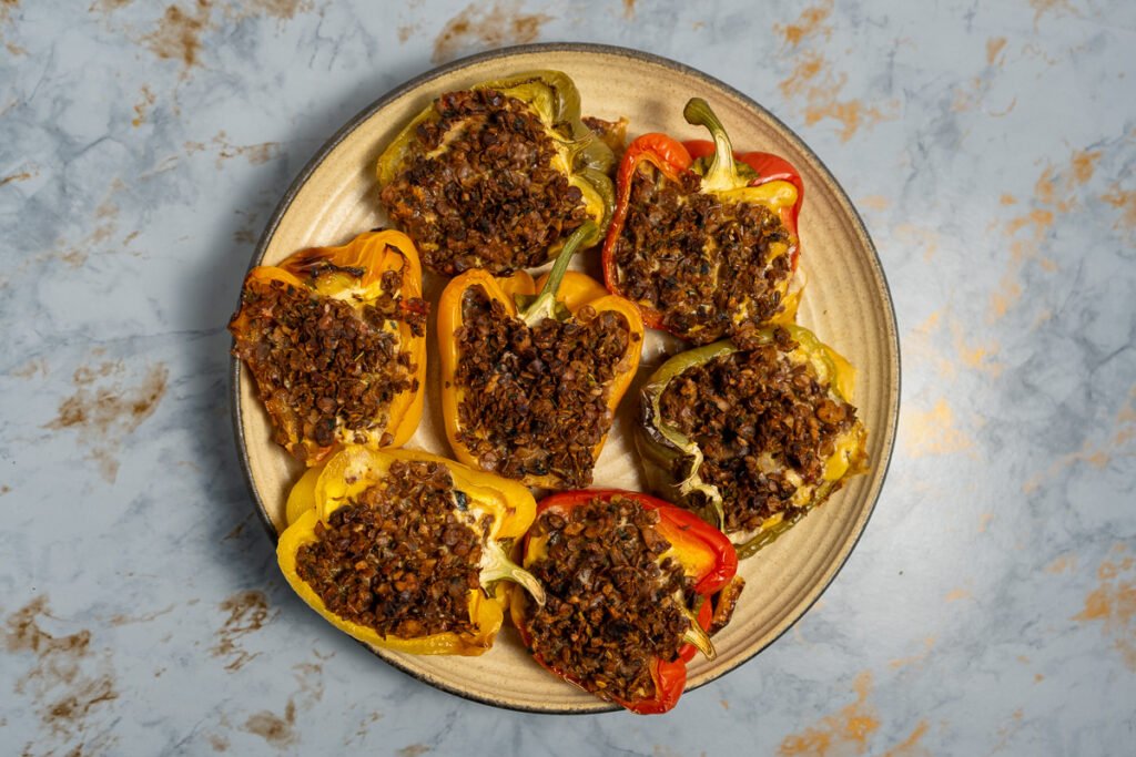 Looking straight down at a plate of 7 bell peppers cut in half lengthwise and stuffed with frittata and vegan sausage.