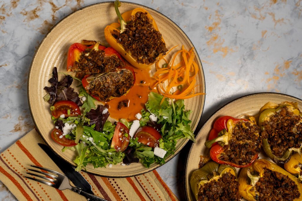 Close up of bell peppers cut in half lengthwise and stuffed with frittata and vegan sausage uncooked on a plate with a side salad.