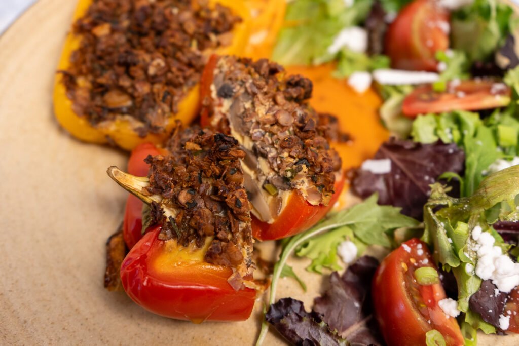 A frittata stuffed bell pepper just in half to reveal the interior which is filled with Just Egg, mushrooms and onions. There is also a side salad on the plate