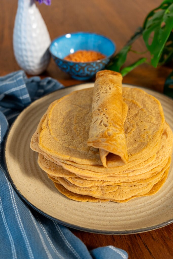 Red lentil wrap rolled up on top of a stack of flat red lentil wraps.