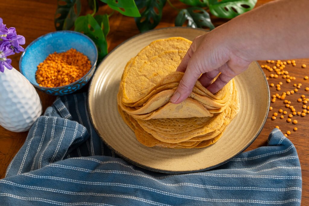 A hand flipping through the stack of red lentil wraps.