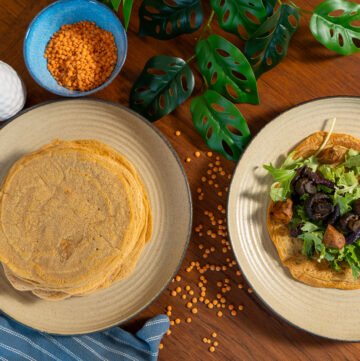 One plate with a large stack of lentil wraps on it to the left, and a plate with a lentil wrap with greens and sweet potatoes on it to the right.