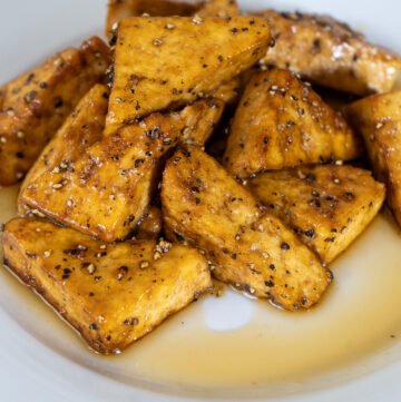 A plate of maple and pepper tofu. The tofu is cut into triangles and stacked in a pile surrounded by maple syrup.