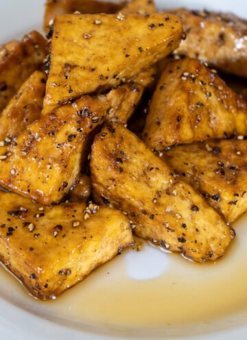 A plate of maple and pepper tofu. The tofu is cut into triangles and stacked in a pile surrounded by maple syrup.