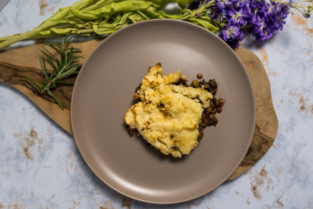 A piece of shepherd's pie on a plate with a purple flower in the background.