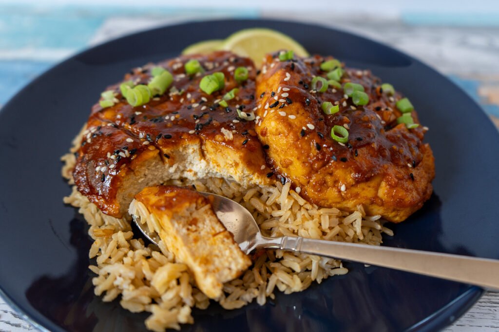 Honey Sriracha Tofu cutlets on a bed of rice with a spoon that cut through it