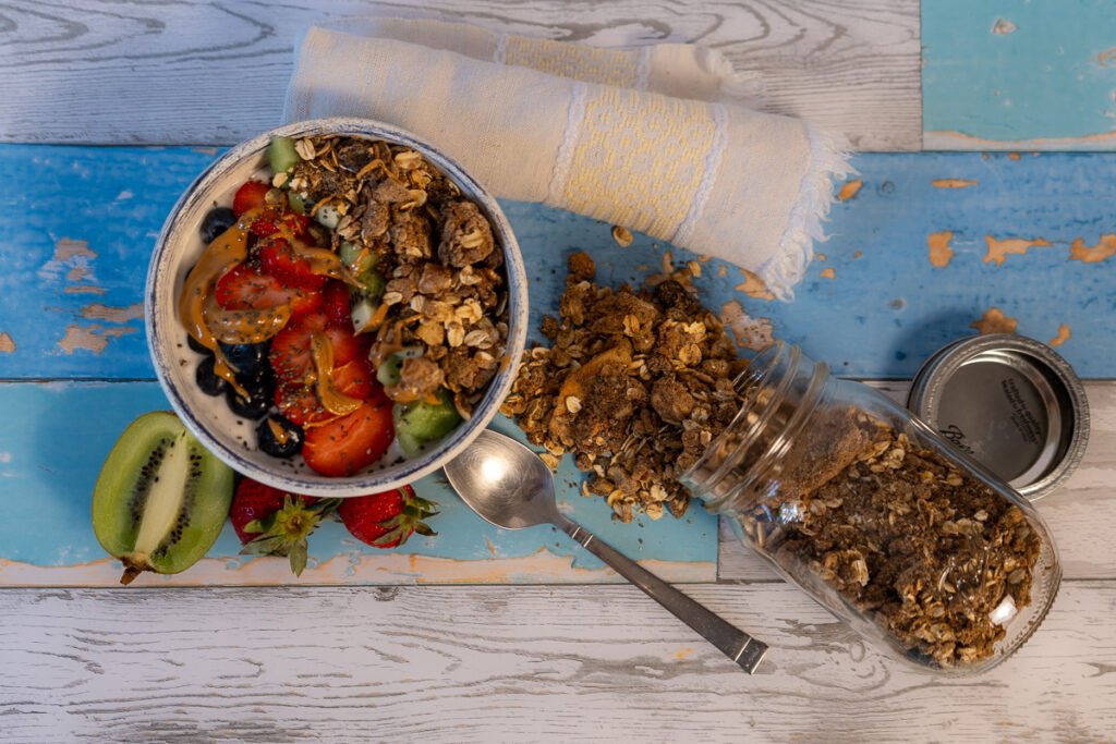 High Protein Vegan Granola spilling out of a mason jar to the right of a bowl of yogurt with the fruit and granola.