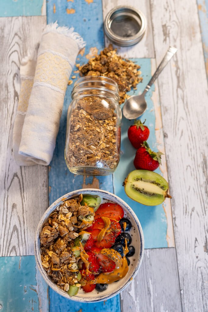 High Protein Vegan Granola spilling out of a mason jar above a bowl of yogurt with the fruit and granola.