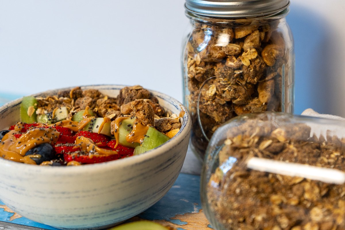 A bowl of yogurt with fruit and granola. Two jars of High Protein Vegan Granola.