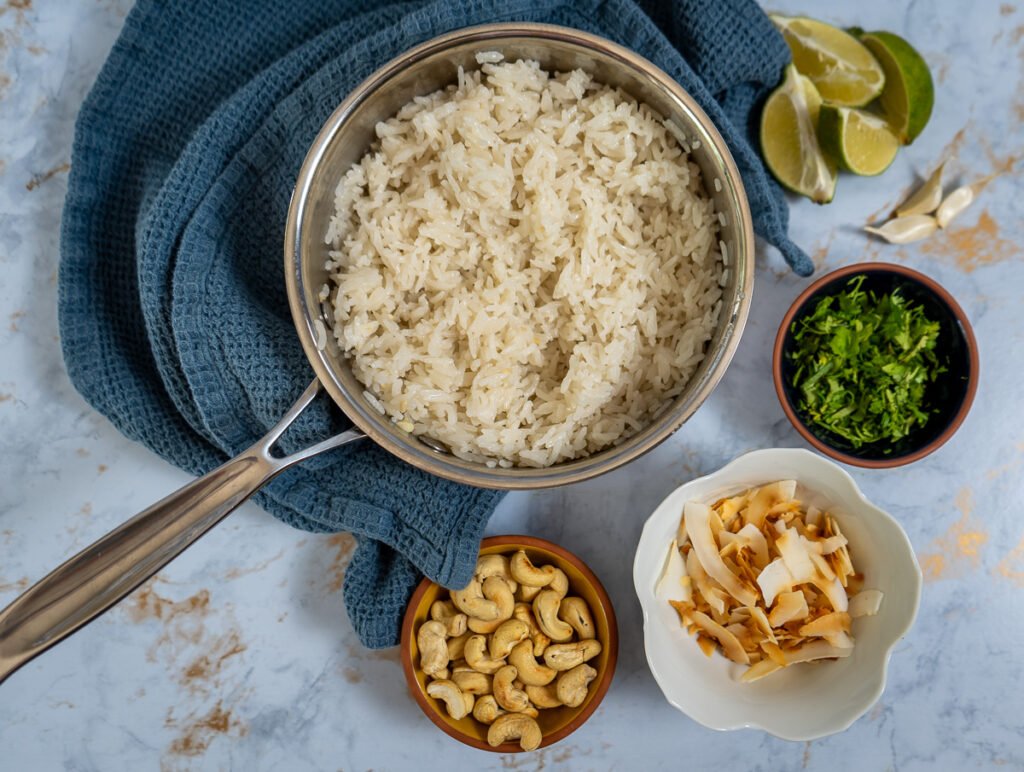 A pot with cooked rice in it and small bowls with cashews, coconut flakes, and cilantro in them.