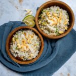 Two bowls of garlic coconut rice with roasted coconut and cashews on top.