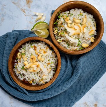 Two bowls of garlic coconut rice with roasted coconut and cashews on top.