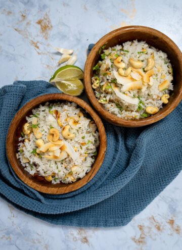 Two bowls of garlic coconut rice with roasted coconut and cashews on top.