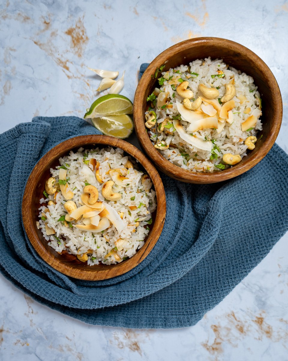 Two bowls of garlic coconut rice with roasted coconut and cashews on top.