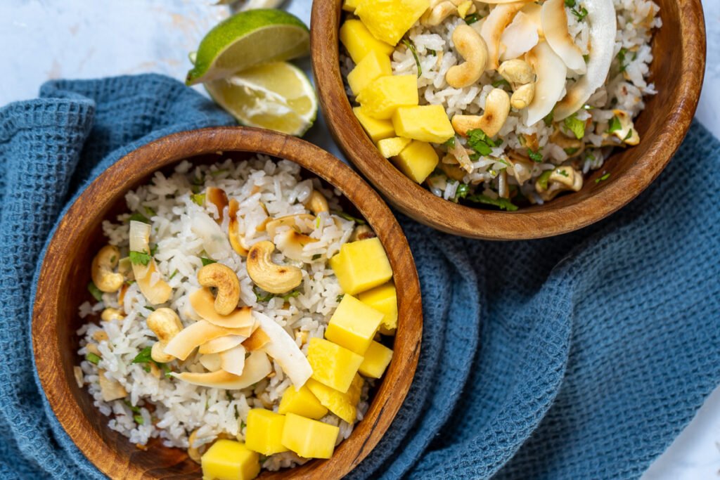 A bowl of garlic coconut rice with roasted coconut and cashews and mangos on top.