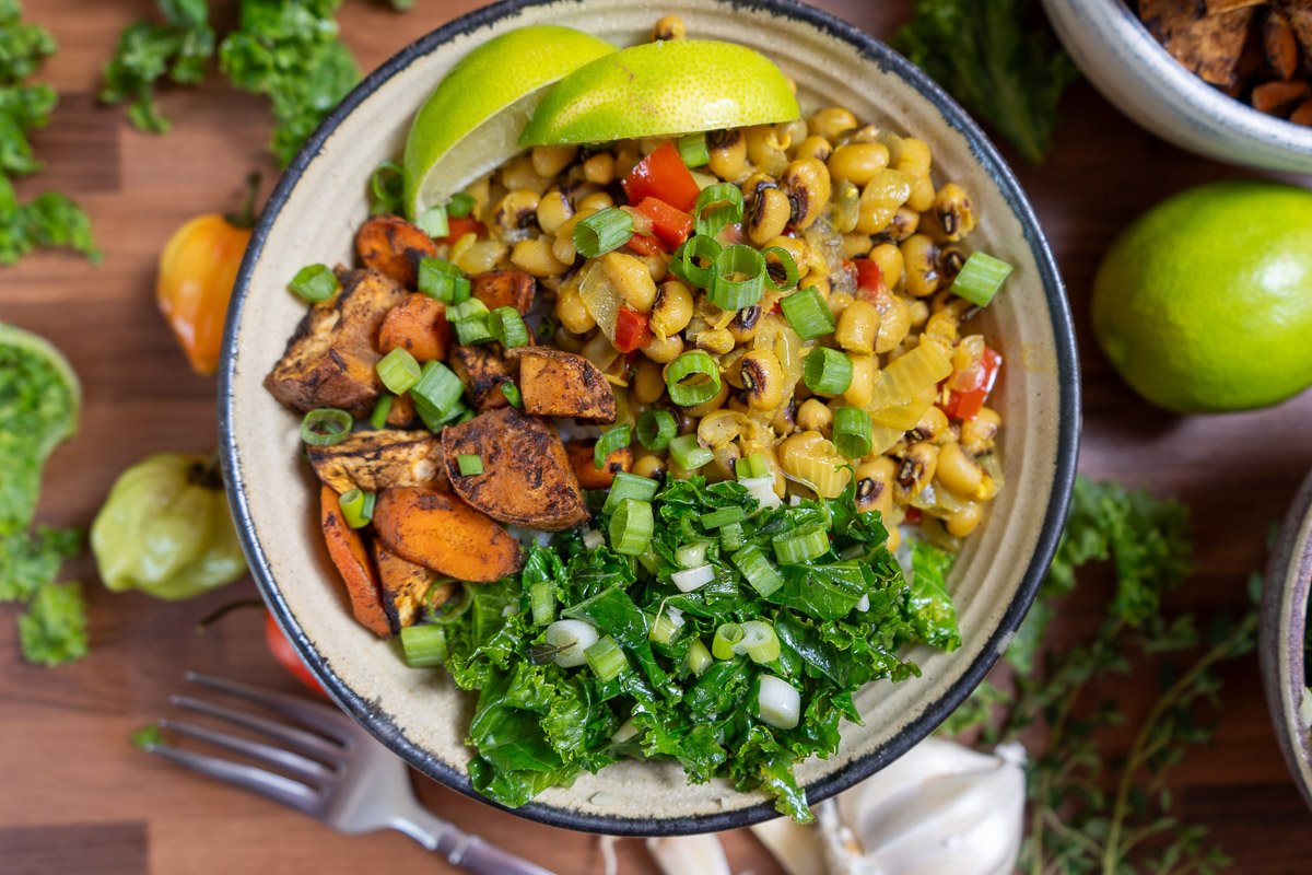 A colorful bowl of Jamaican black eyed pea curry, jerk sweet potatoes and carrots, and garlic kale.