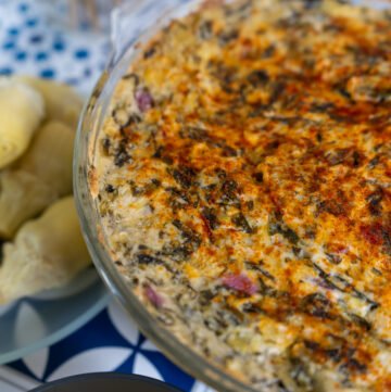 Spinach Artichoke dip in a glass casserole dish and a plate of artichoke hearts to the side