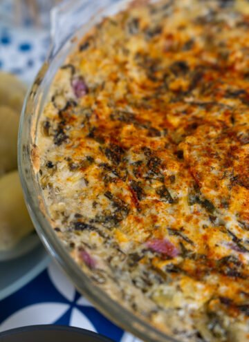 Spinach Artichoke dip in a glass casserole dish and a plate of artichoke hearts to the side