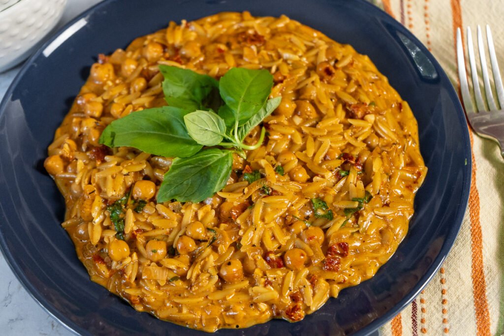 Creamy Marry Me Chickpea orzo with basil garnish on a blue plate.