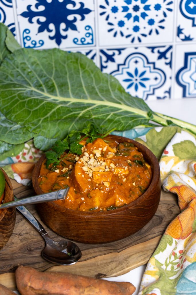 A bowl if West African Peanut stew in a wooden bowl. There is a big collard green leaf in the background.